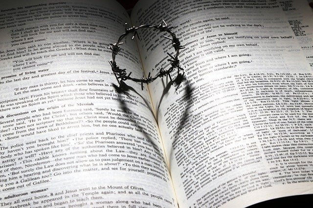 Aufgeschlagene Bibel auf der eine Dornenkrone liegt. Der Schatten der Dornenkrone bildet ein Herz auf den aufgeschlagenen Seiten der Bibel.